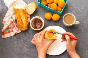 closeup woman hand is eating apricot jam slice bread with milk cup