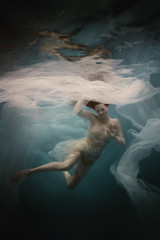 Fototapeta na wymiar Girl in a white dress with a cloth swims underwater