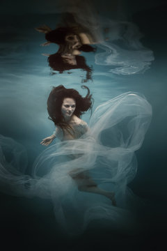 Girl in a white dress with a cloth swims underwater