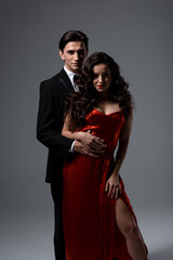passionate couple in suit and red silk dress hugging on grey