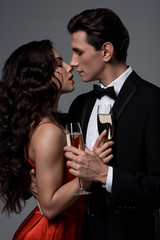 Romantic couple holding champagne glasses and going to kiss, isolated on grey