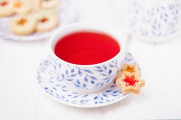 Pink fruit tea and homemade cookie star with jam on a white wooden background