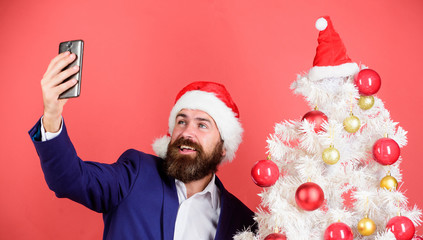 manager santa hat use smartphone. selfie near xmas tree. Capture happy memory. new year party. merry christmas. bearded man search gift online. businessman working on holidays. greeting his nearest