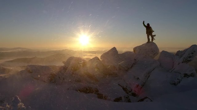 Aerial view: Freerider stands on top of the mountain, snowboard in hand. movable camera plans. Fresh powder. Extreme freeride skiers skiing from the top. beautiful storm of snow flying in the frame