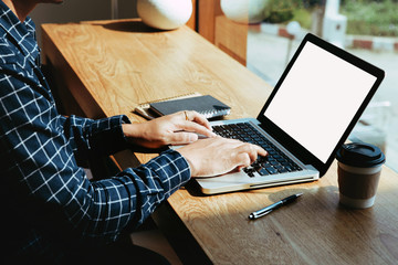 Man's hands using laptop with blank screen on desk in coffee shop.