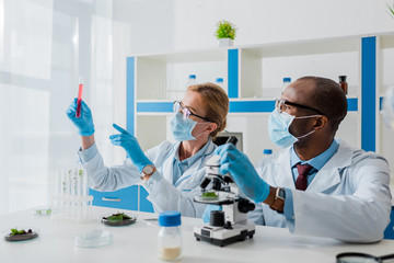 multicultural biologists pointing with finger and looking at test tube in lab