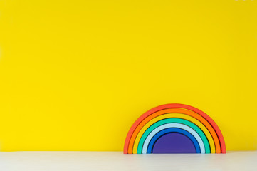 Wooden toy rainbow on the shelf on yellow background