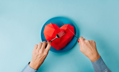 Female hands eating paper volume heart on blue background