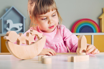 Little girl playing with wooden toy rocket from galaxy balancer