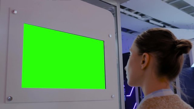 Green screen, mockup, future, copyspace, template, chroma key, technology concept. Woman looking at blank digital interactive green display wall at exhibition or museum with futuristic sci-fi interior