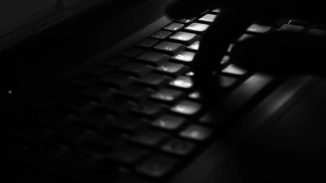 Close up of a male fingers, typing on the keyboard in the darkness.