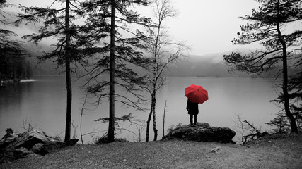 Wanderung um den Eibsee am Fuß der Zugspitze. Wanderer mit rotem Regenschirm. Bild in schwarz...
