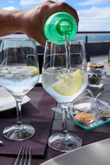 Drinking cold mineral water with bubbles, served in wine glass with ice cubes and lemon