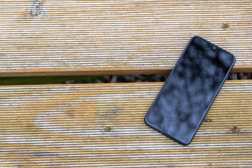 Schwarzes Smartphone Phablet liegt auf einem Holztisch im Garten und zeigt mit copy space mobile...