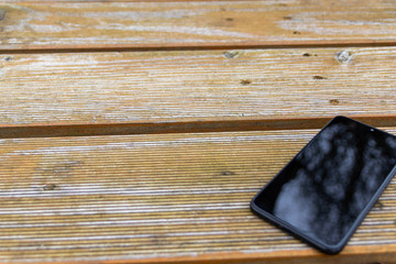 Schwarzes Smartphone Phablet liegt auf einem Holztisch im Garten und zeigt mit copy space mobile...