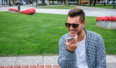 Young man sitting on a park bench sending audio message with mobile