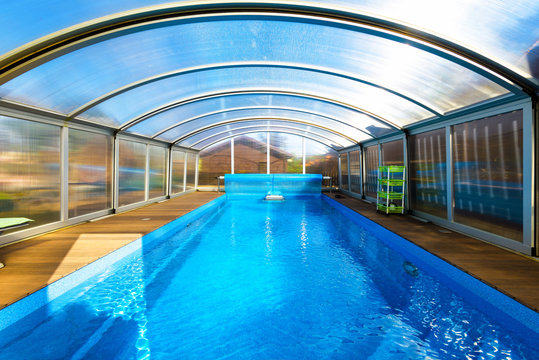 Swimming pool with blue water and transparent plastic tent. Modern pool design with collapsible wall and ceiling.