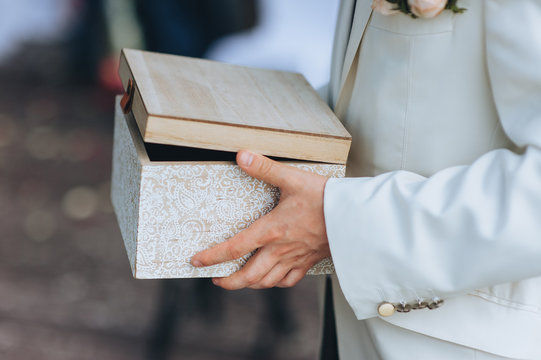 A man in a beige suit holds a wooden box with a gift. Hands and casket for collecting money close-up. Wedding ceremony, holiday. Photography, concept.