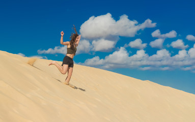 ein M&auml;dchen rennt im Sommer voller Lebensfreude von einer Sandd&uuml;ne und wirbelt dabei Staub auf