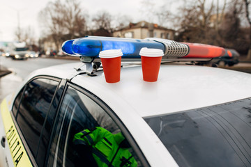 Two hot drink cups on a car of a patrol crew outdoors. Coffee, tea cups on a police car. 