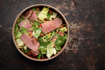 Green salad with beef pastrami and honey mustard sauce. Food, ready dish on a dark background. Suggestion of serving the dish.