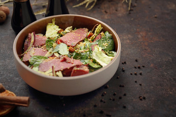 Green salad with beef pastrami and honey mustard sauce. Food, ready dish on a dark background. Suggestion of serving the dish.