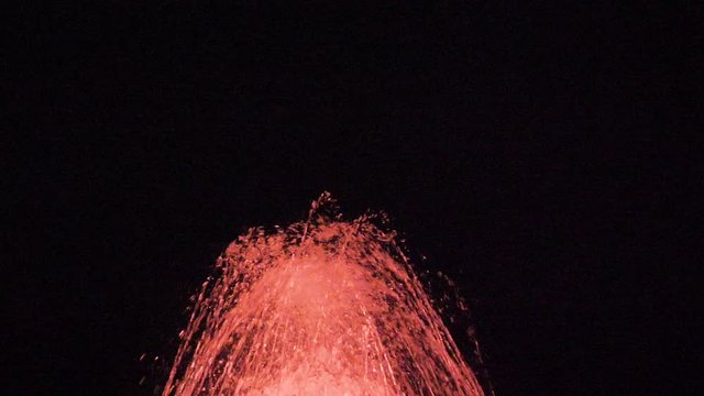 slow otion tilt shot of water fountain lit by red lights
