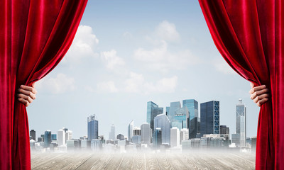 Business city in gray fog behind red curtain and hand holding it