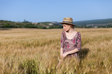 Naklejka na ściany i meble portrait of a beautiful fashionable blonde woman in a hat in a field of ripe wheat