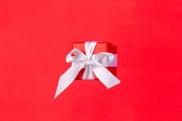Red gift box with white satin ribbon bow flying on red background. Minimal concept for christmas...
