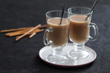Indian masala tea with milk, spices and cinnamon and biscuits straws on a dark gray background