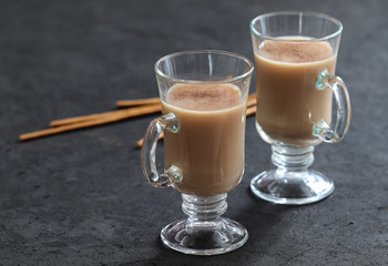 Indian masala tea with milk, spices and cinnamon and biscuits straws on a dark gray background
