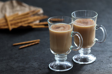 Indian masala tea with milk, spices and cinnamon and biscuits straws on a dark gray background