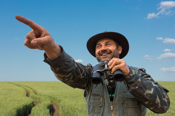 A man with a gun in his hands and an orange vest on a pheasant hunt in a wooded area in cloudy...