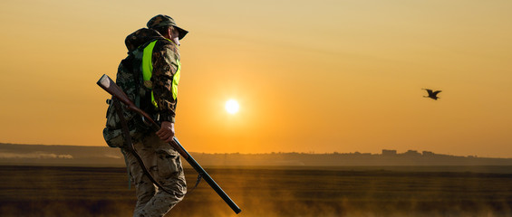 A man with a gun in his hands and an orange vest on a pheasant hunt in a wooded area in cloudy...