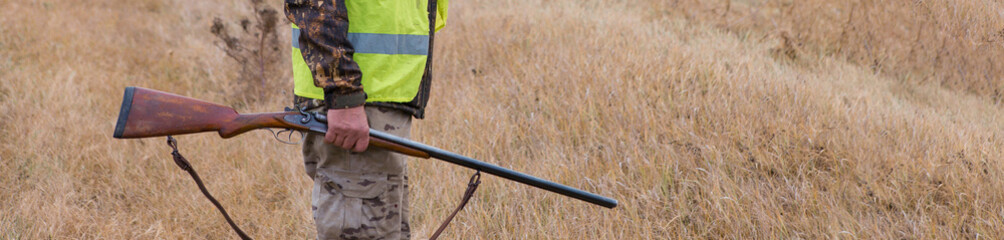 A man with a gun in his hands and an orange vest on a pheasant hunt in a wooded area in cloudy...