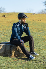 Cyclist in pants and fleece jacket on a modern carbon hardtail bike with an air suspension fork rides off-road. The guy is resting on a stump in the park, looks into the distance.