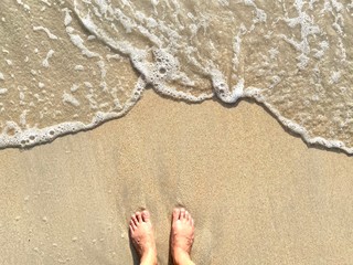 The feet of young women not wearing shoes, stand on fine sand. Have bubbles or waves break but still not touch the feet. At sea in the daytime. Good rest allow the body to touch nature on good holiday