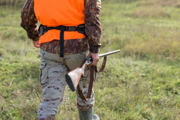 A man with a gun in his hands and an orange vest on a pheasant hunt in a wooded area in cloudy...