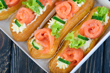 Tasty and beautiful eclairs on a wooden board. Appetizing dessert with red fish, cucumber, cheese and greens.