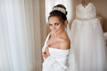 The morning of the bride. Portrait of a brunette bride in a white silk coat behind a dress