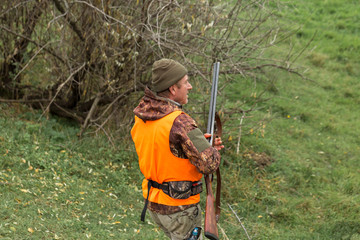 Hunting period, autumn season open. A hunter with a gun in his hands in hunting clothes in the autumn forest in search of a trophy.
