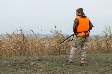 Hunting period, autumn season open. A hunter with a gun in his hands in hunting clothes in the autumn forest in search of a trophy.