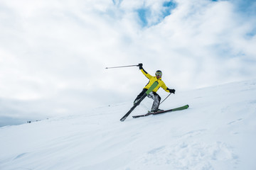 Fototapeta na wymiar excited sportsman holding ski sticks and skiing on white slope