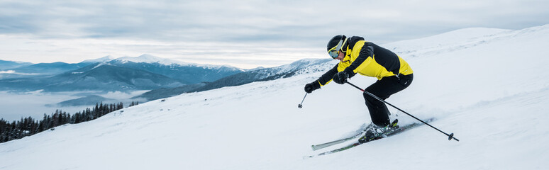 Fototapeta premium panoramic shot of sportsman skiing on slope in mountains