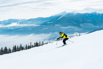 Naklejka na ściany i meble sportsman holding sticks and skiing on slope with snow in mountains