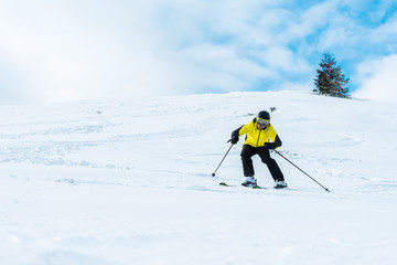 Fototapeta na wymiar sportsman in helmet skiing on slope against sky with clouds