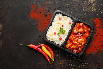 Box diet. Chicken in Mexican sauce with rice. Ready dish in a black container. Composed take-out meal, diet catering. The container on a dark background.