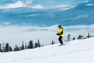 Naklejka na ściany i meble skier in helmet holding sticks and skiing on slope in wintertime