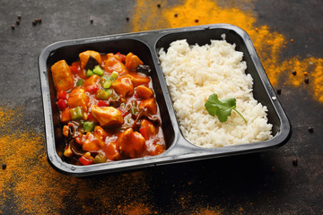 Box diet, Chinese chicken with white rice. Ready dish in a black container. Composed take-out meal, diet catering. The container on a dark background.